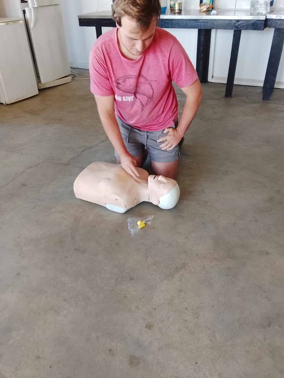 Student kneeling and practising CPR on a training mannequin during first aid course