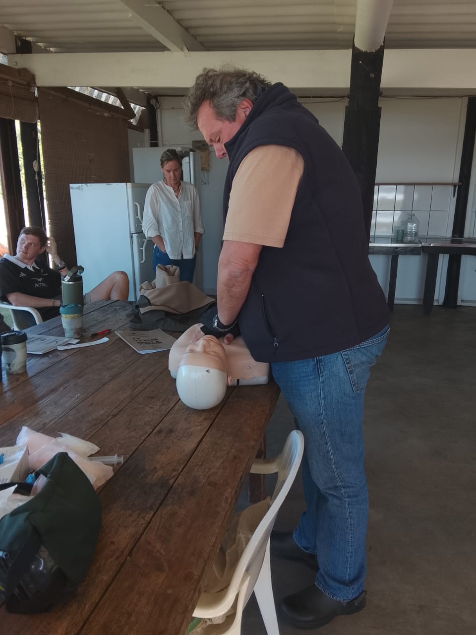 Instructor demonstrating CPR technique on a mannequin at a table with students observing